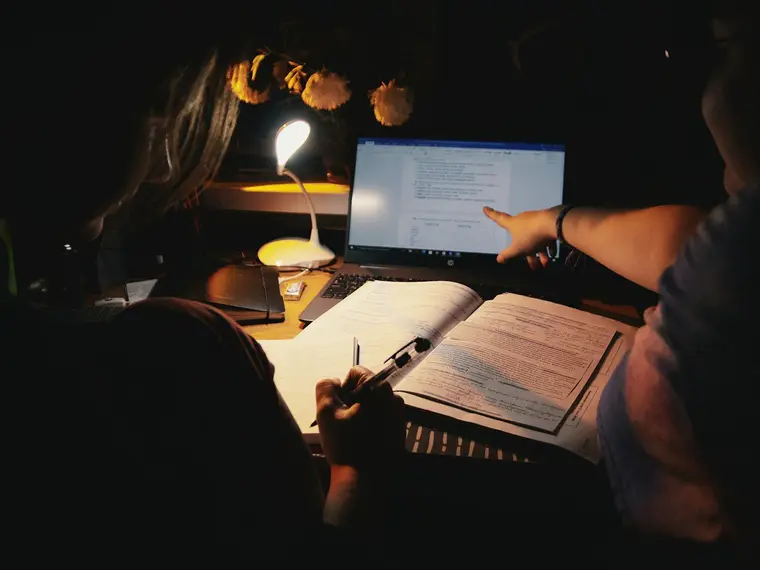 Uczeń przy biurku nocą z lampką, laptopem i zeszytem