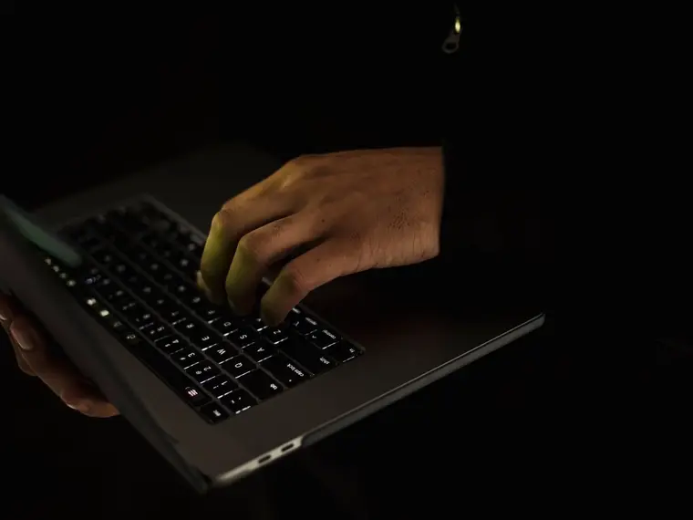 Dłonie piszące na klawiaturze laptopa w ciemnym pokoju