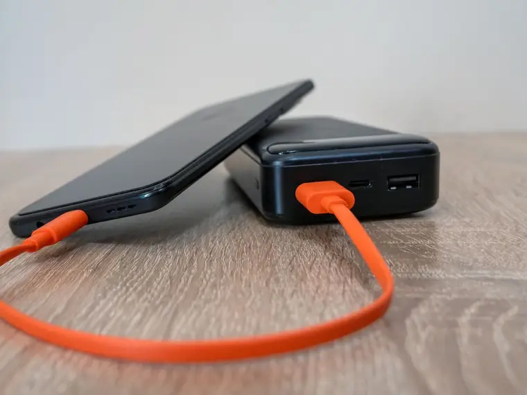 Powerbank ładujący telefon pomarańczowym kablem